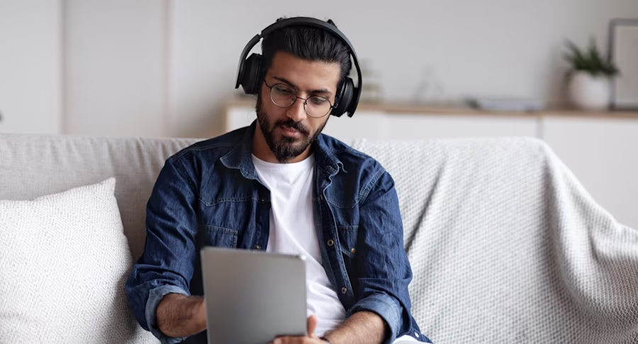 Man sitting on sofa wearing head phone and using laptop