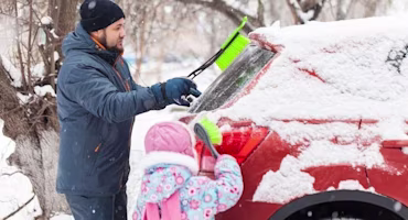 Man and daughter brushing snow off car