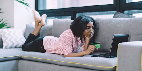 a woman on a sofa looking at a laptop holding a credit card