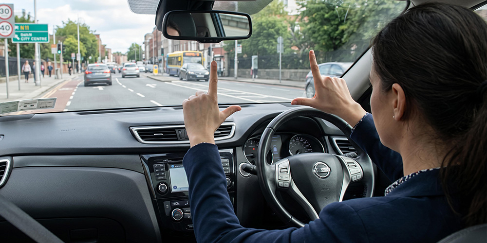 female driver holding hands out in front of her in 'L' formations