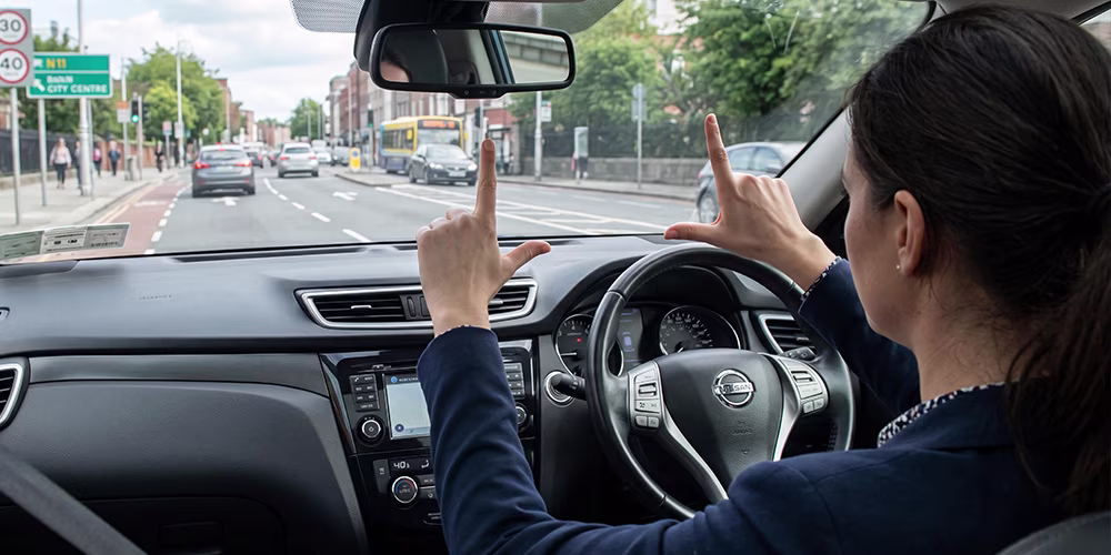 female driver holding hands out in front of her in 'L' formations