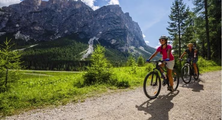 Two people cycling a trail next to a mountain