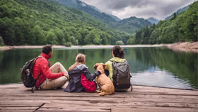 A family with a dog sitting on the edge of a lake and looking at the scenery