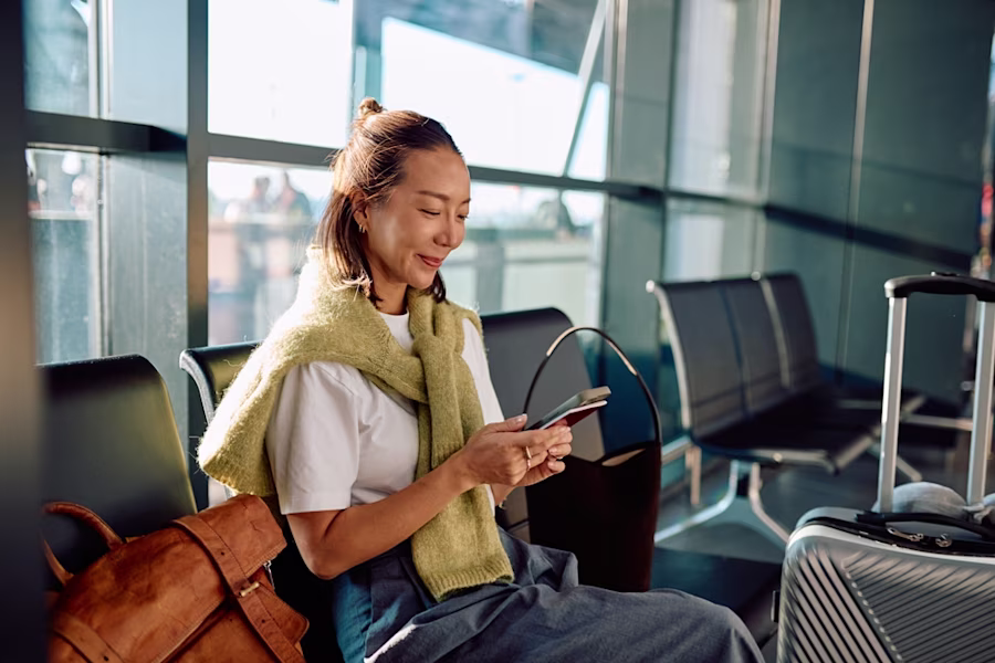 Woman waiting at departure gate looking at phone smiling