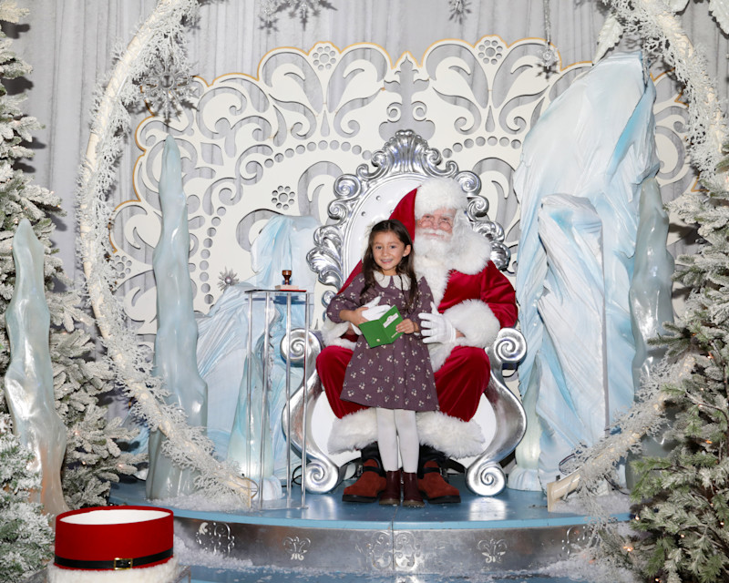 Child visiting Santa in a snowy silver sleigh set at Passport to Santa
