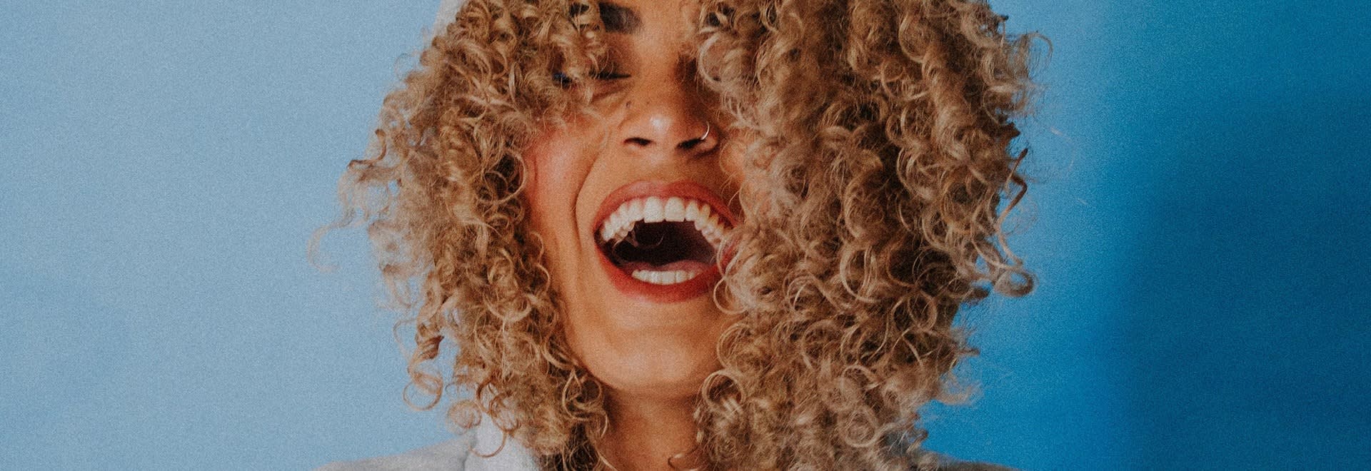 A portrait photo of a woman with blonde curly hair laughing to the camera