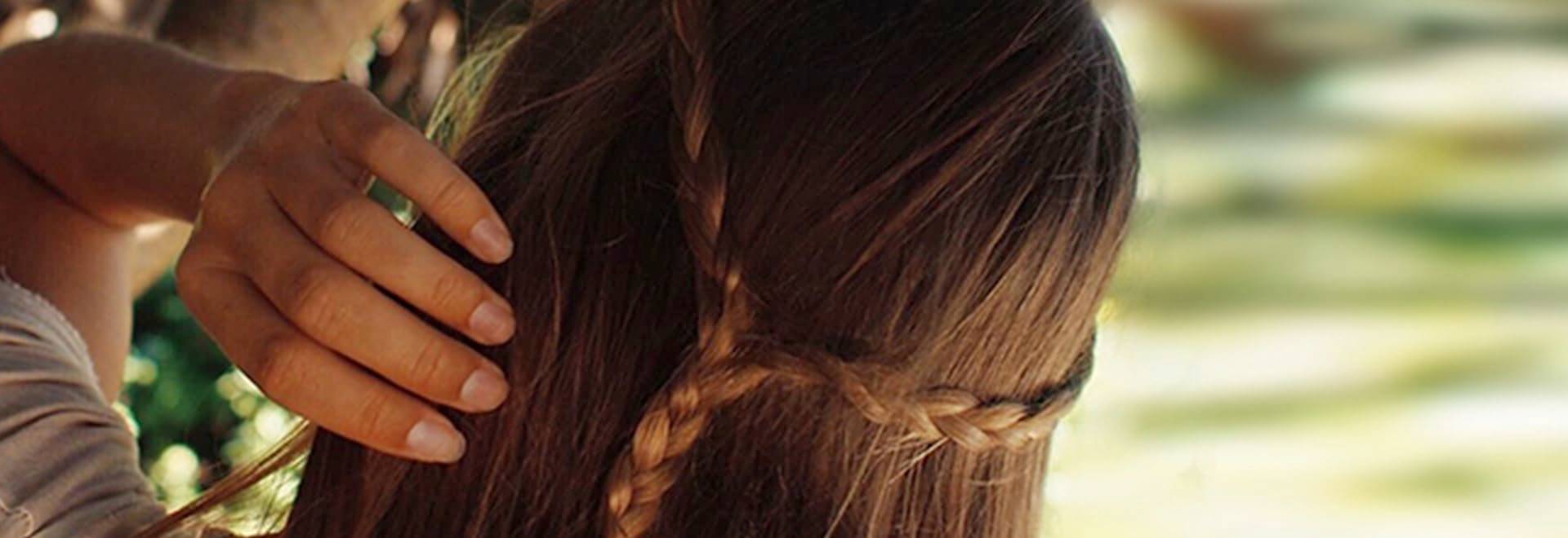 A woman with a dark-blonde braid made of part of her hair touching her head and standing backwards to the camera
