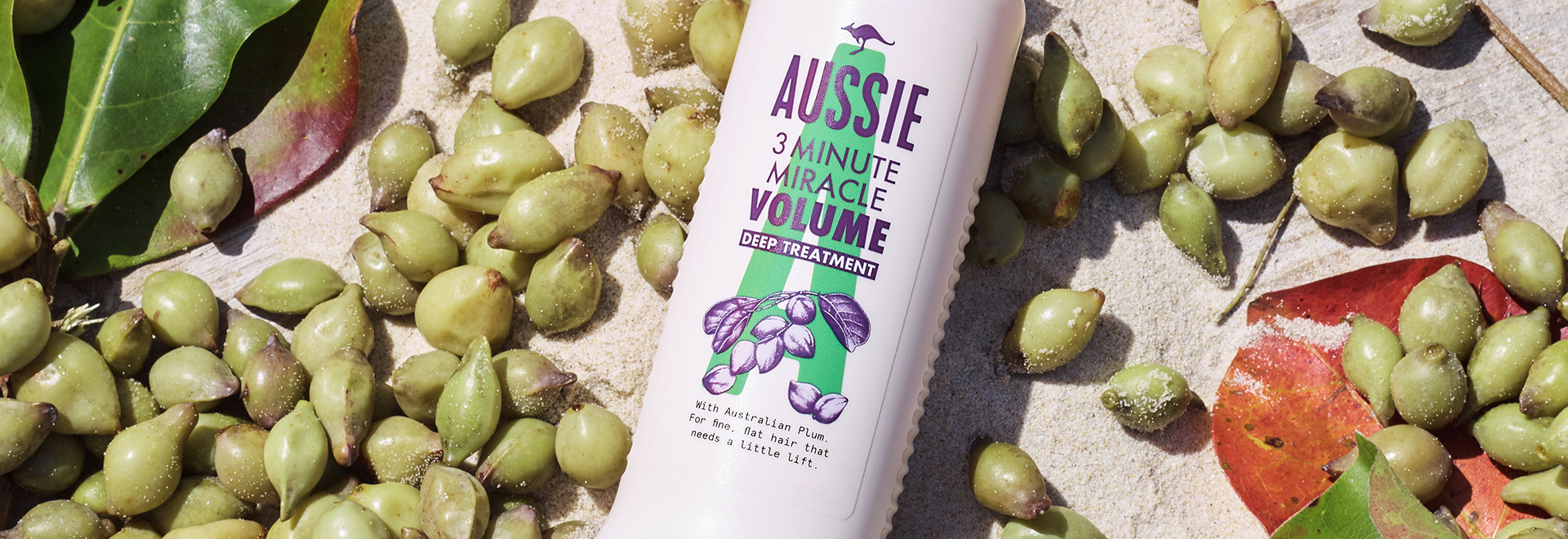 A Aussie Shampoo bottle surrounded by kakadu plums on the sand 