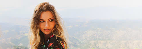 A photo of a woman with long blonde hair looking oin her side on the mountaing background
