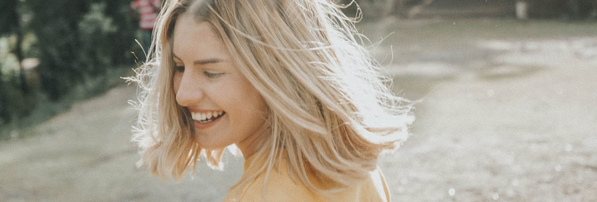 A photo of a woman with middle-lenght blonde hair smiling and throwing her hair around her head