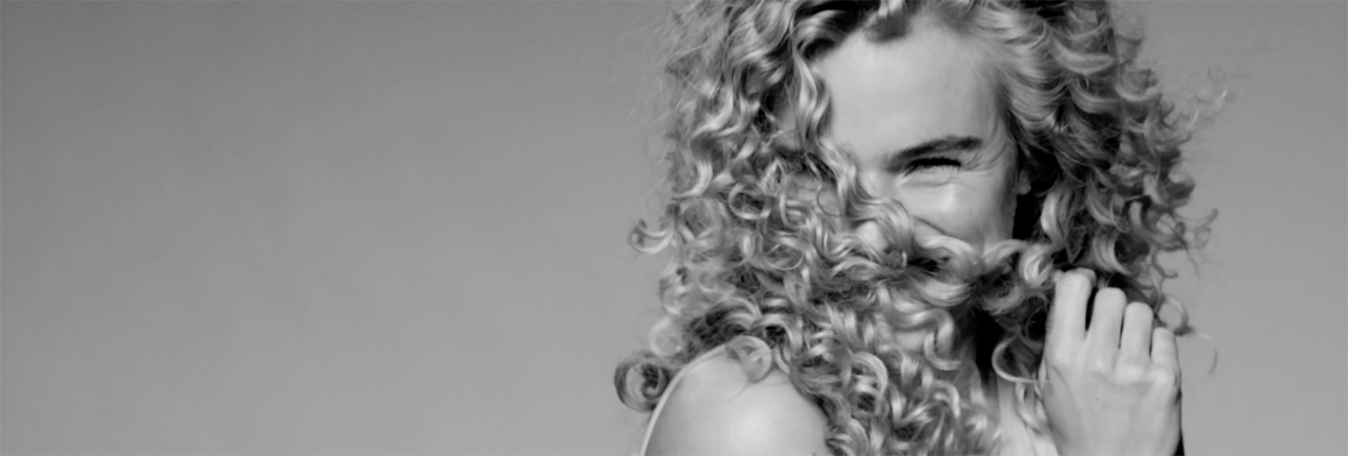 A black and white photo of a girl with long curls hiding her face behind her hair