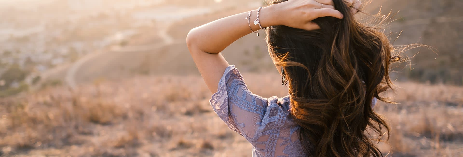 A photo of woman touching her head standing backwards to the camera and a town in a village in the background