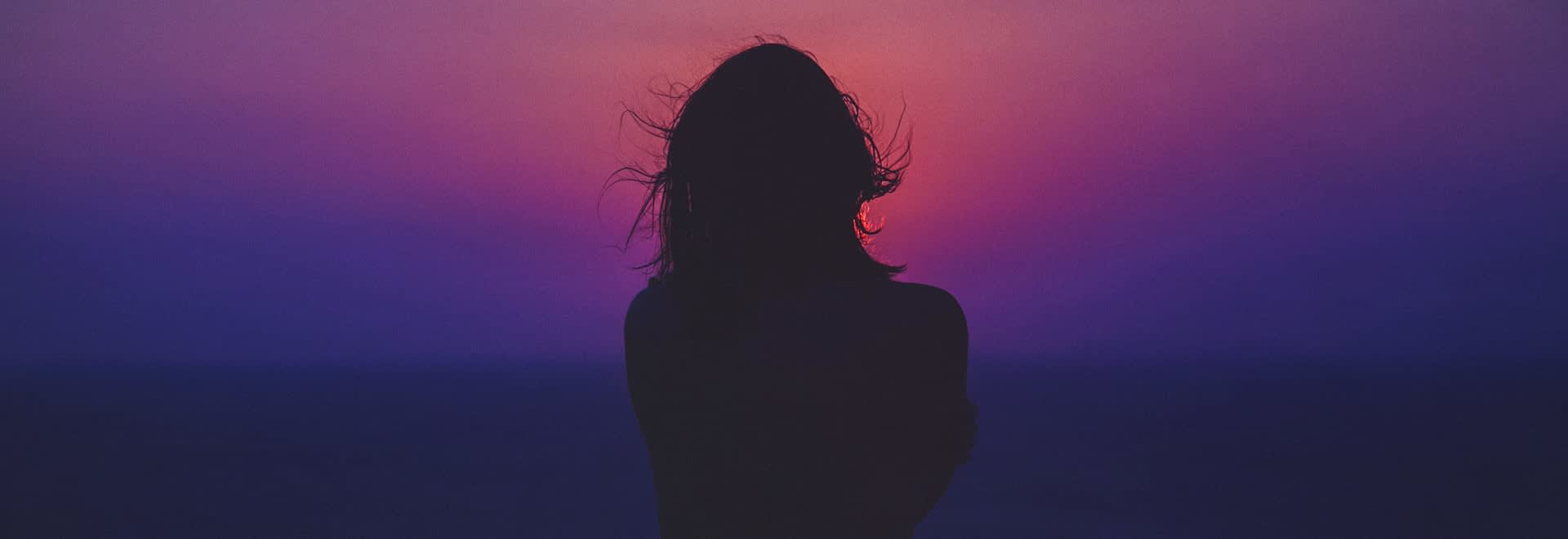 A woman's shape on the dark purple sunset background