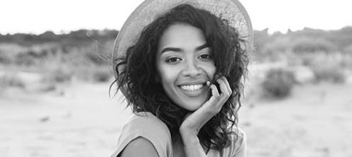 Black and white portrait of a woman with dark, curly hair with hat on