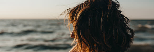 A photo of a woman with middle-lenght borwn hair watching the sea during the sunset