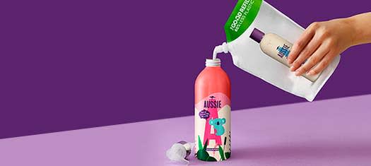 A picture of Aussie Aluminium Shampoo Bottle and a hand pouring a shampoo to the bottle from refill package on the pinky-purple background