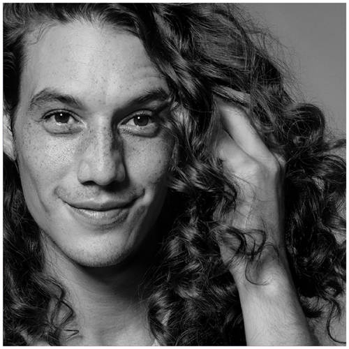 A black and white portrait of a man with long curly hair.