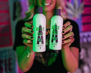 A photo of a woman's hands presenting two Bottles of Aussie Frizz Shampoo