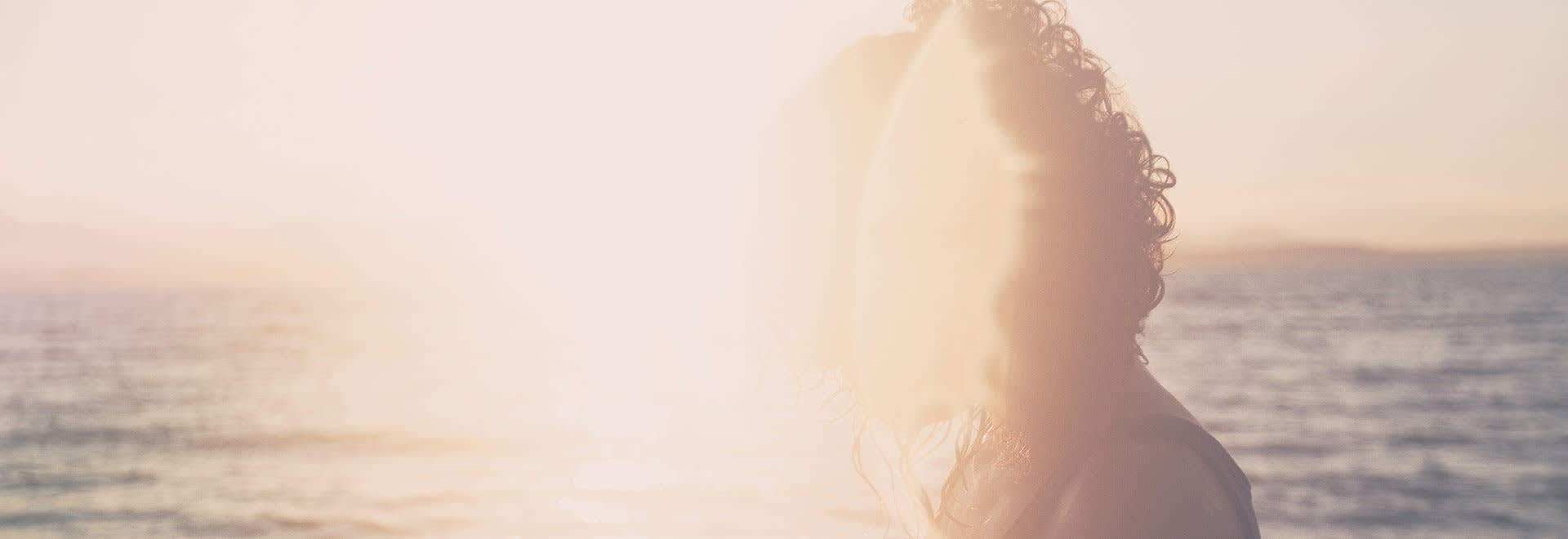 A photo of woman's shape with a sunlight hitting the camera and a sunset in the background