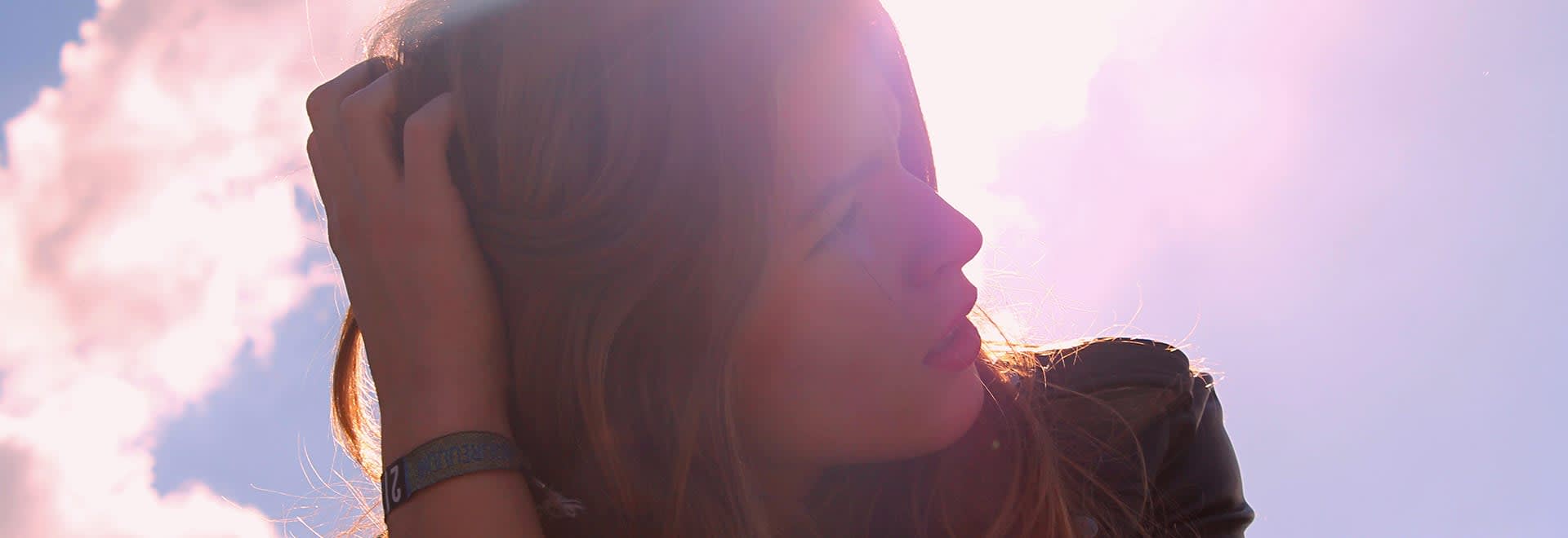 A photo of woman touching her head with a sunlight hitting the camera and a sunset in the background