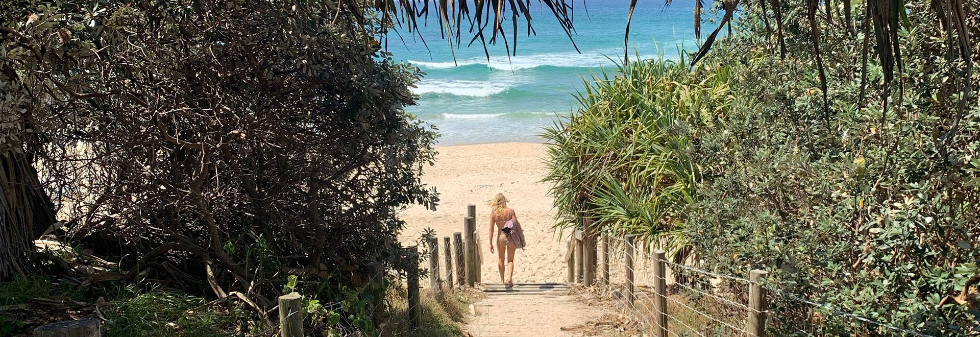 A photo of beach landscape with a girl in a swimsuit in the middle who is going towards the ocean
