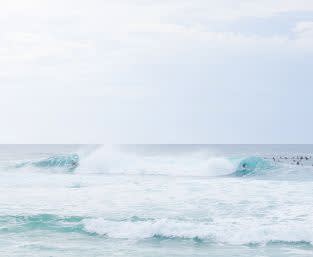 A photo of the ocean, one big wave and people in the water