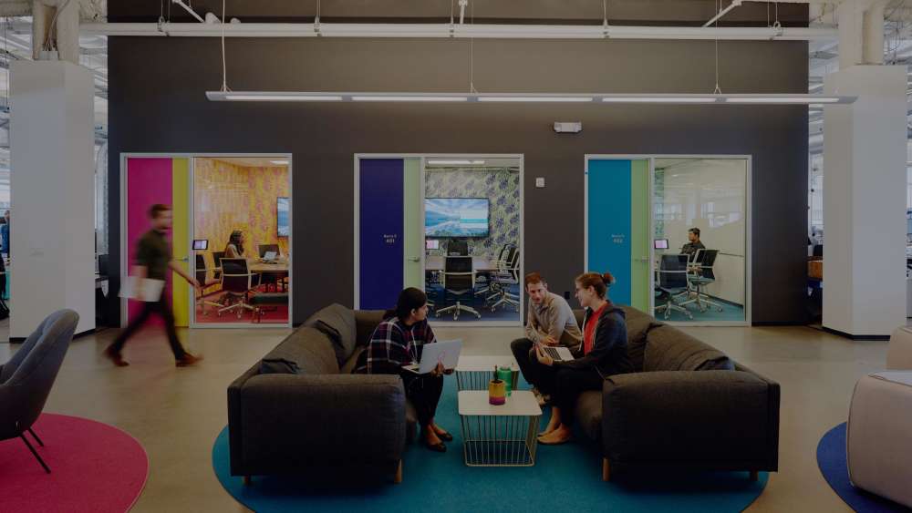 Image of Lyft employees sitting on two couches facing each other in Lyft office with conference rooms in the background.  
