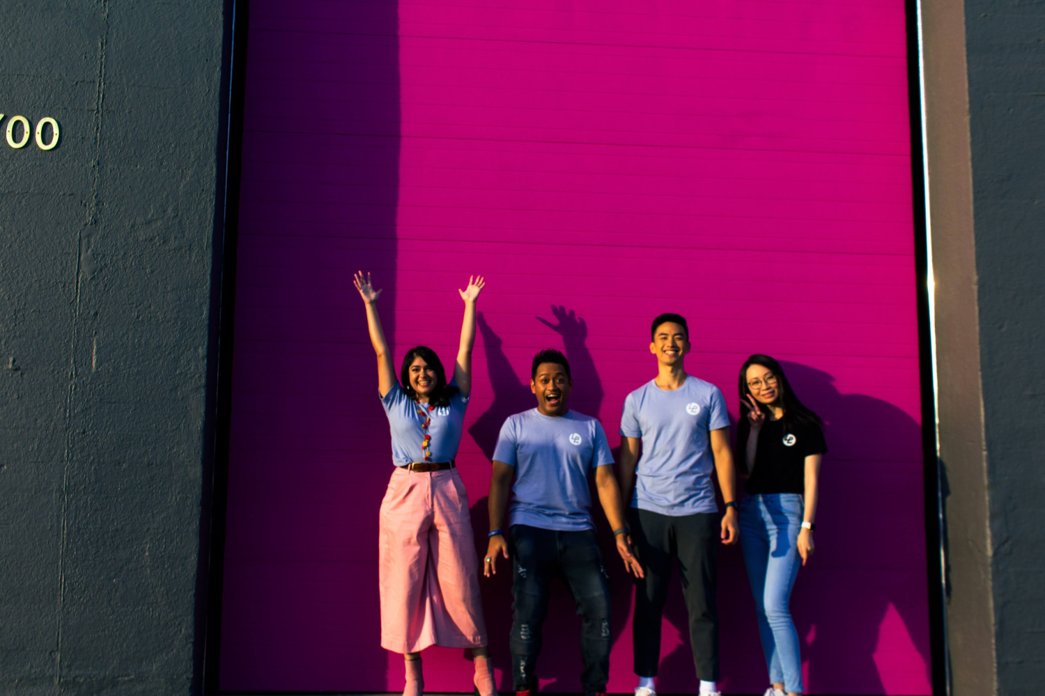 Four Lyft systems designers pose for a photo against a pink background during a team offsite.