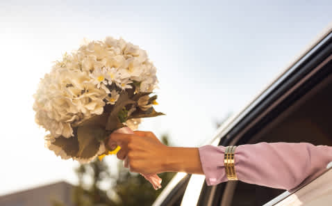 a woman holding out a bouquet of flowers out a car window