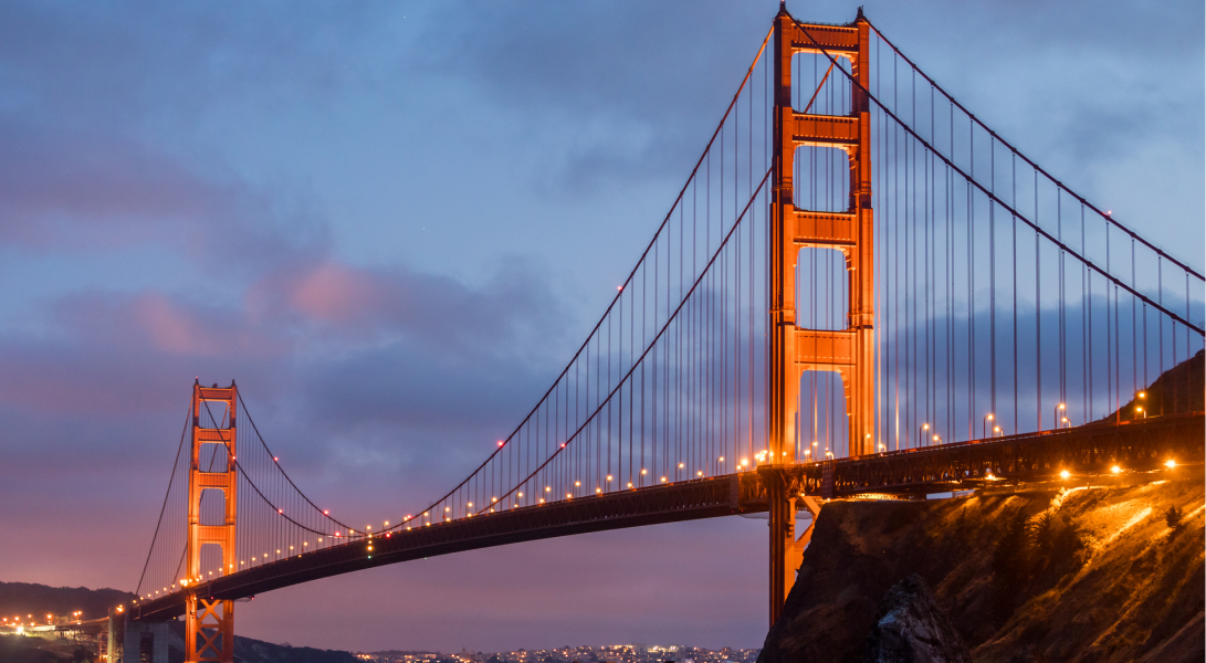 Golden Gate Bridge at dusk with orange lights, purple sky, and city lights in the background.