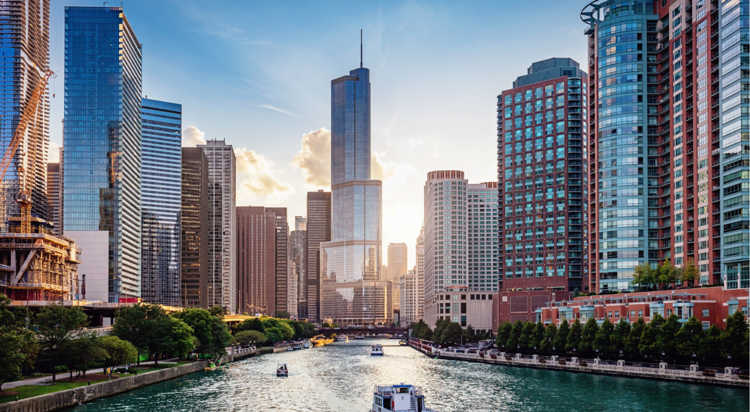 Downtown Chicago skyline with tall glass buildings, river, boats, and trees. 