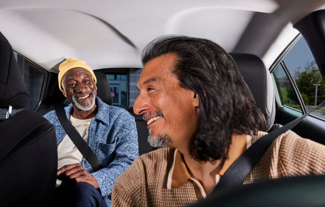 Image of smiling driver looking back at a smiling passenger in a car.  