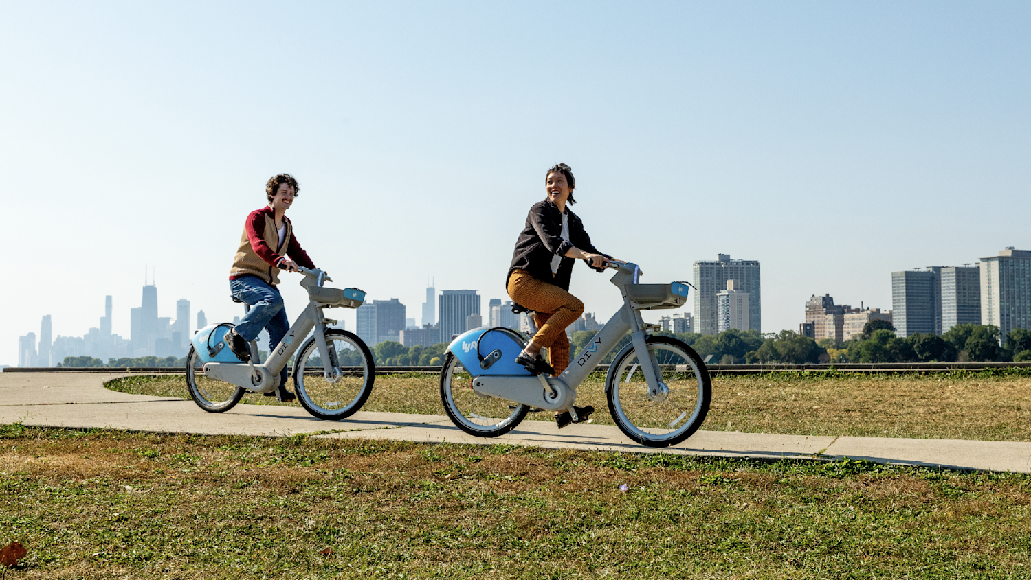 Person in a red hat rides a blue Divvy bike past a white tiled wall on a sunny day.