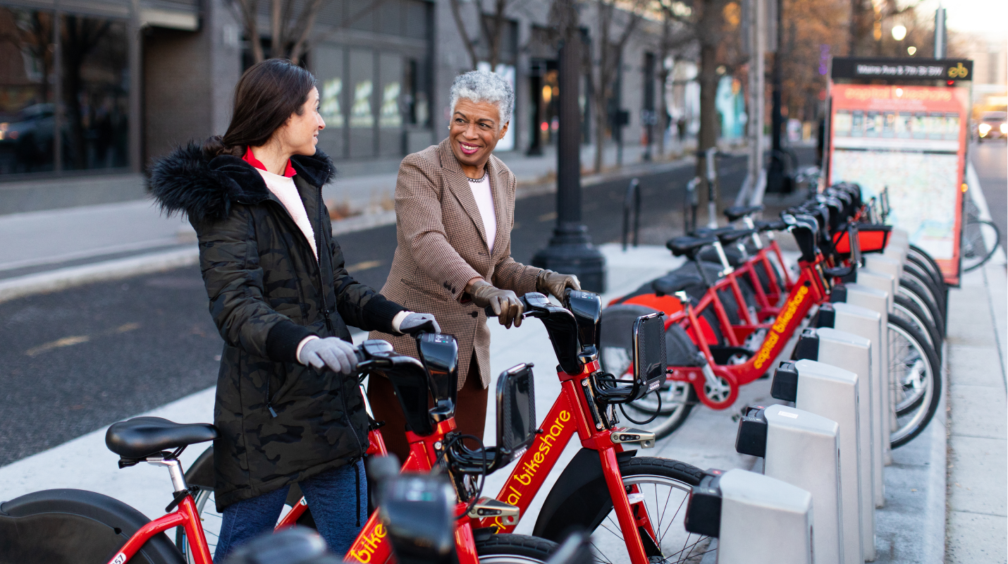Two women smiling while picking up bikes at a Capital Bikeshare station. 