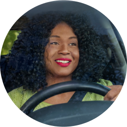 Monica, a Lyft driver, sits in the driver’s seat, smiling. Her hand is on the steering wheel.