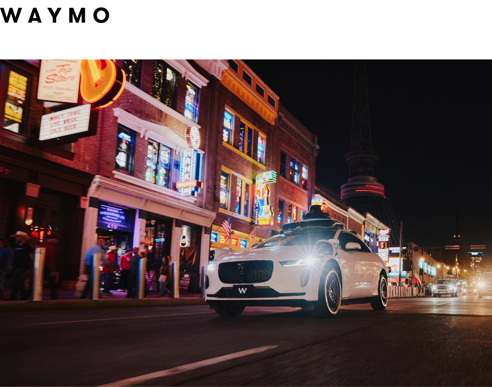 White Jaguar E-PACE drives on a city street at night with buildings and lights.