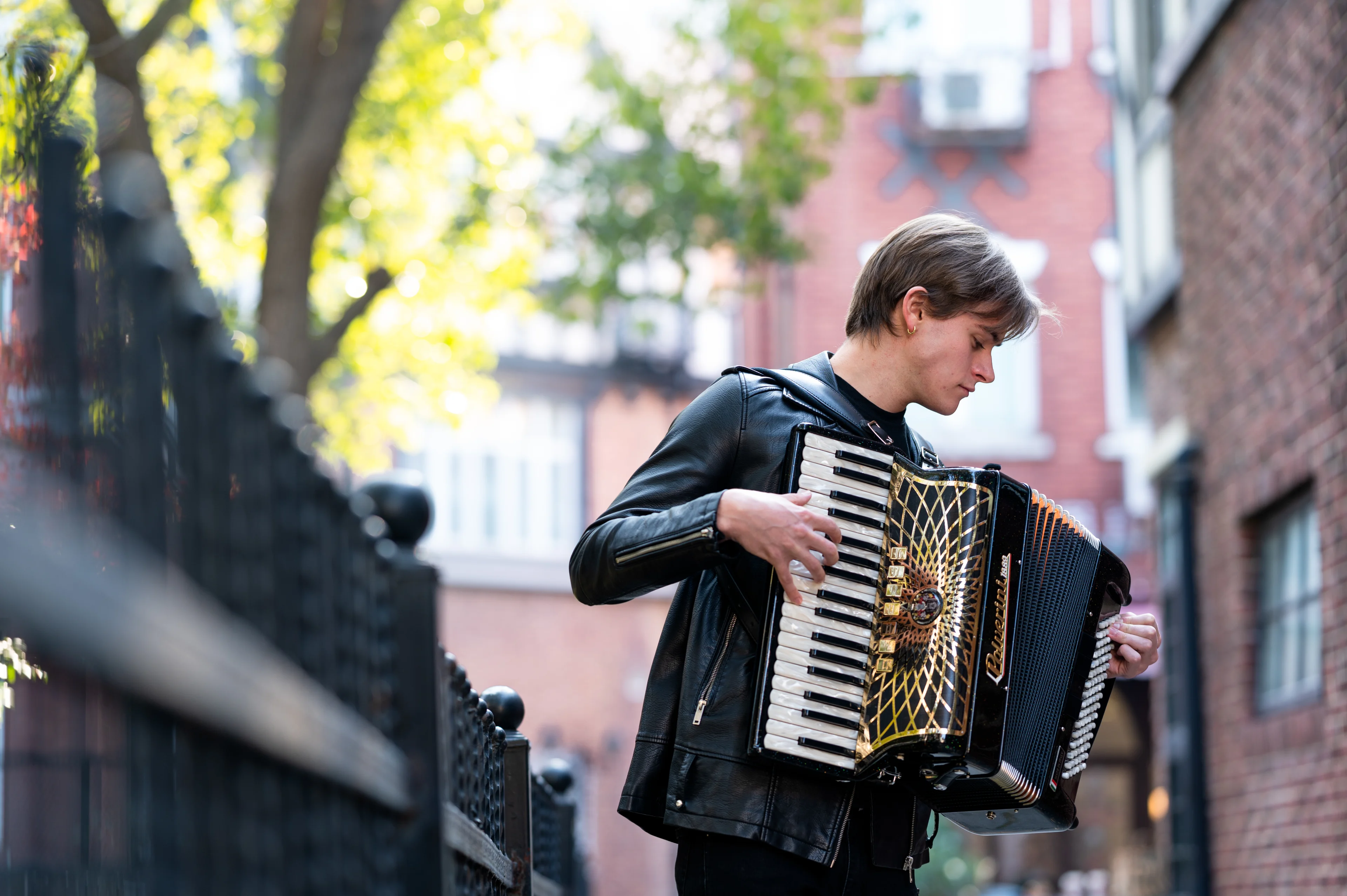 Man playing black Polverini accordion by a fence.