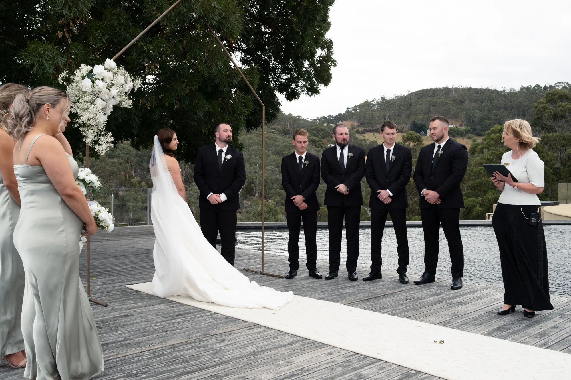 Mary Figg leading a wedding ceremony beside a reflective pool, bridal party and guests looking on