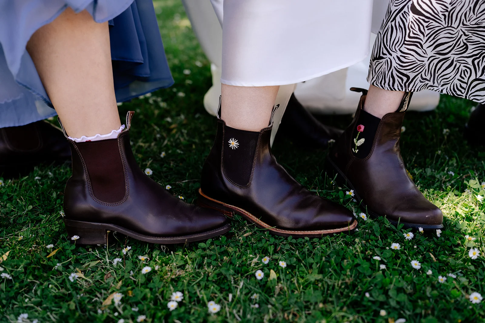Three pairs of Blundstone boots in the grass among daisies at an outdoor Tasmanian wedding