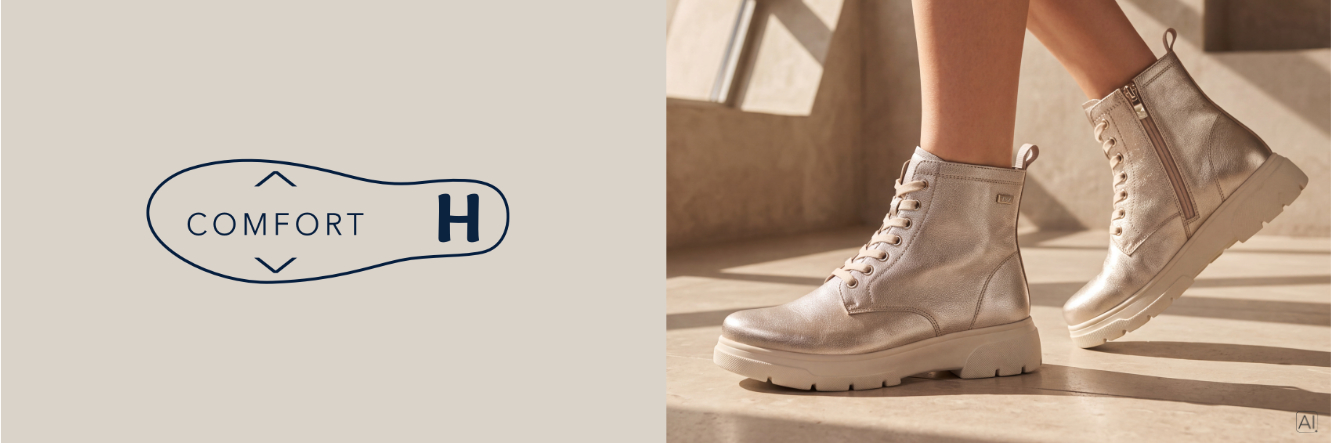 Donna bionda in abito beige si siede sul muretto con sandali Caprice Comfort davanti a uno scenario mediterraneo con case bianche e mare
