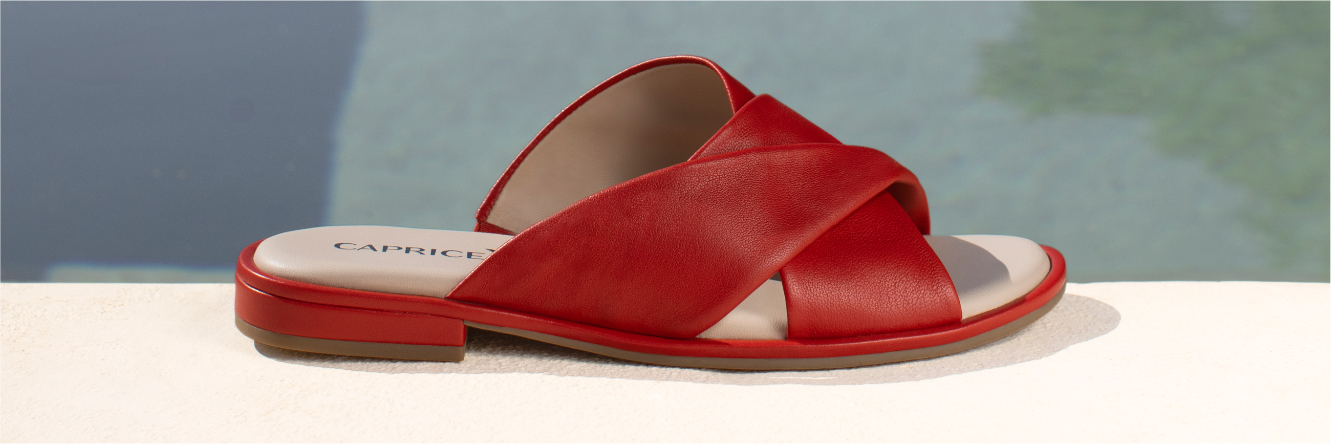 Mules in pelle rossa con cinturini incrociati su sfondo chiaro con sfondo sfocato