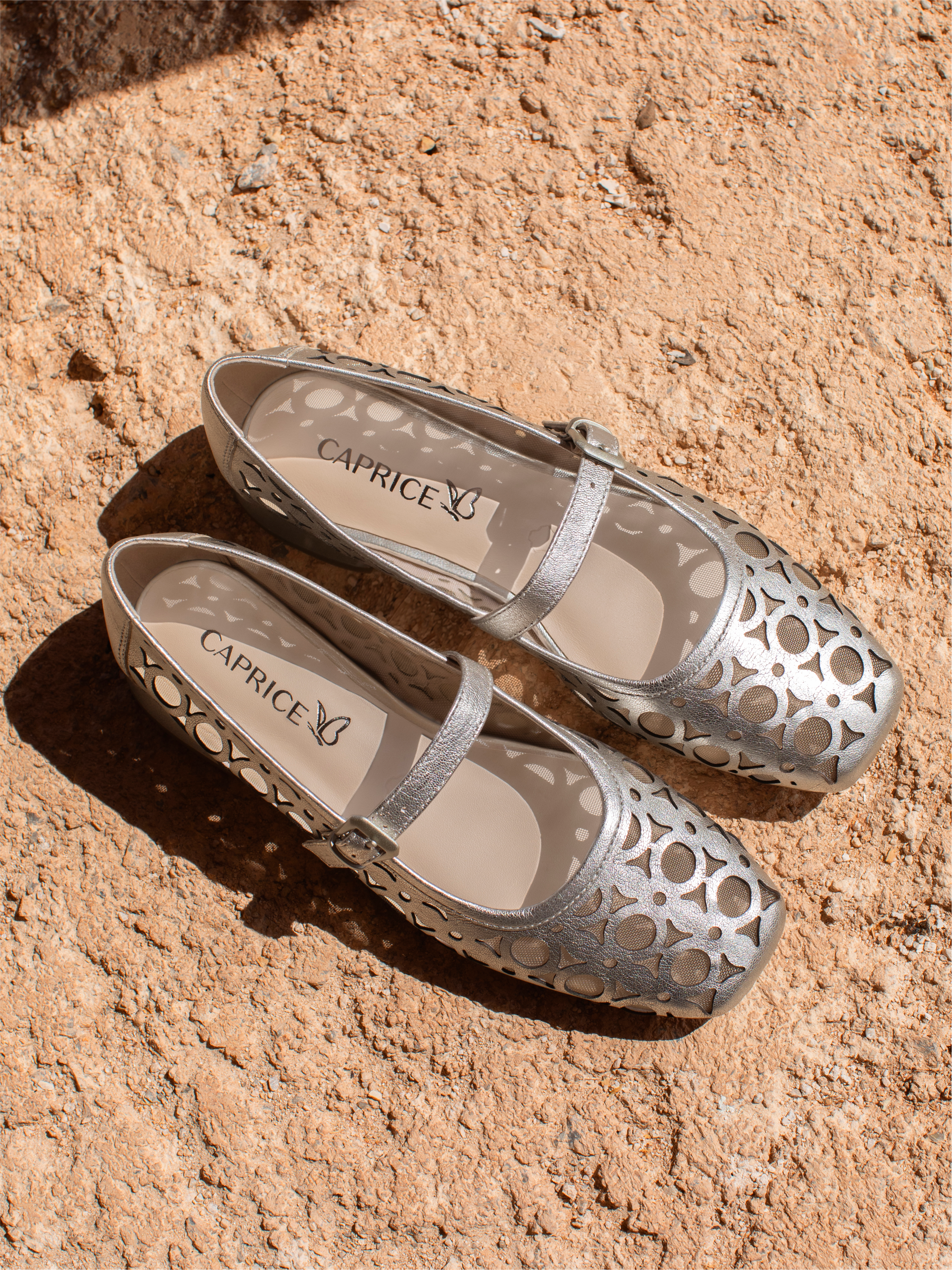 Ballerines Caprice argentées avec motif ajouré sur fond de sable au soleil