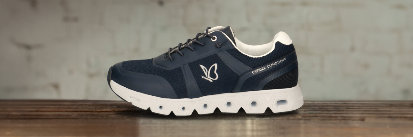 Chaussure de sport bleu foncé avec semelle blanche et logo Caprice Airmotion en forme de papillon sur une surface en bois sur un fond gris