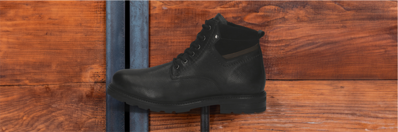 Zwarte leren laars met vetersluiting voor een roodbruine houten wand