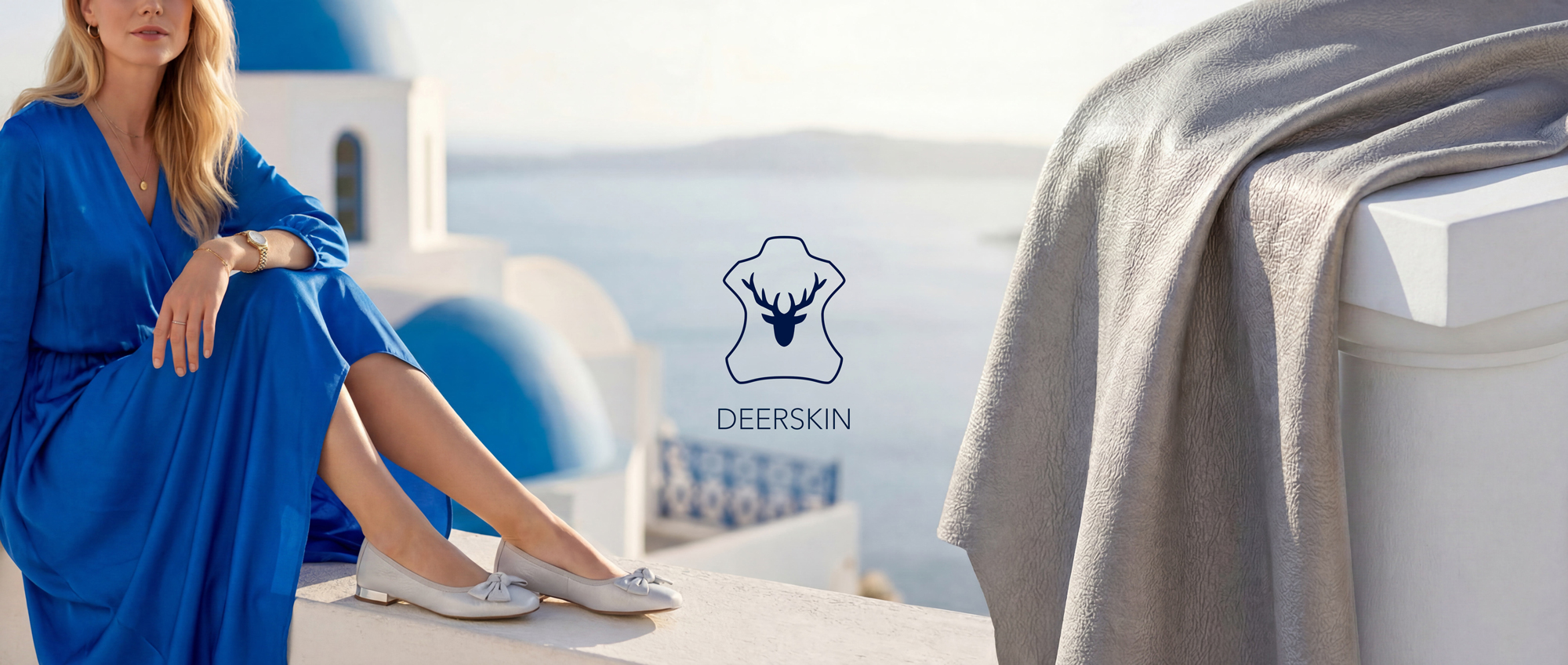 Woman in blue dress sits next to Deerskin logo in front of Mediterranean backdrop with sea view