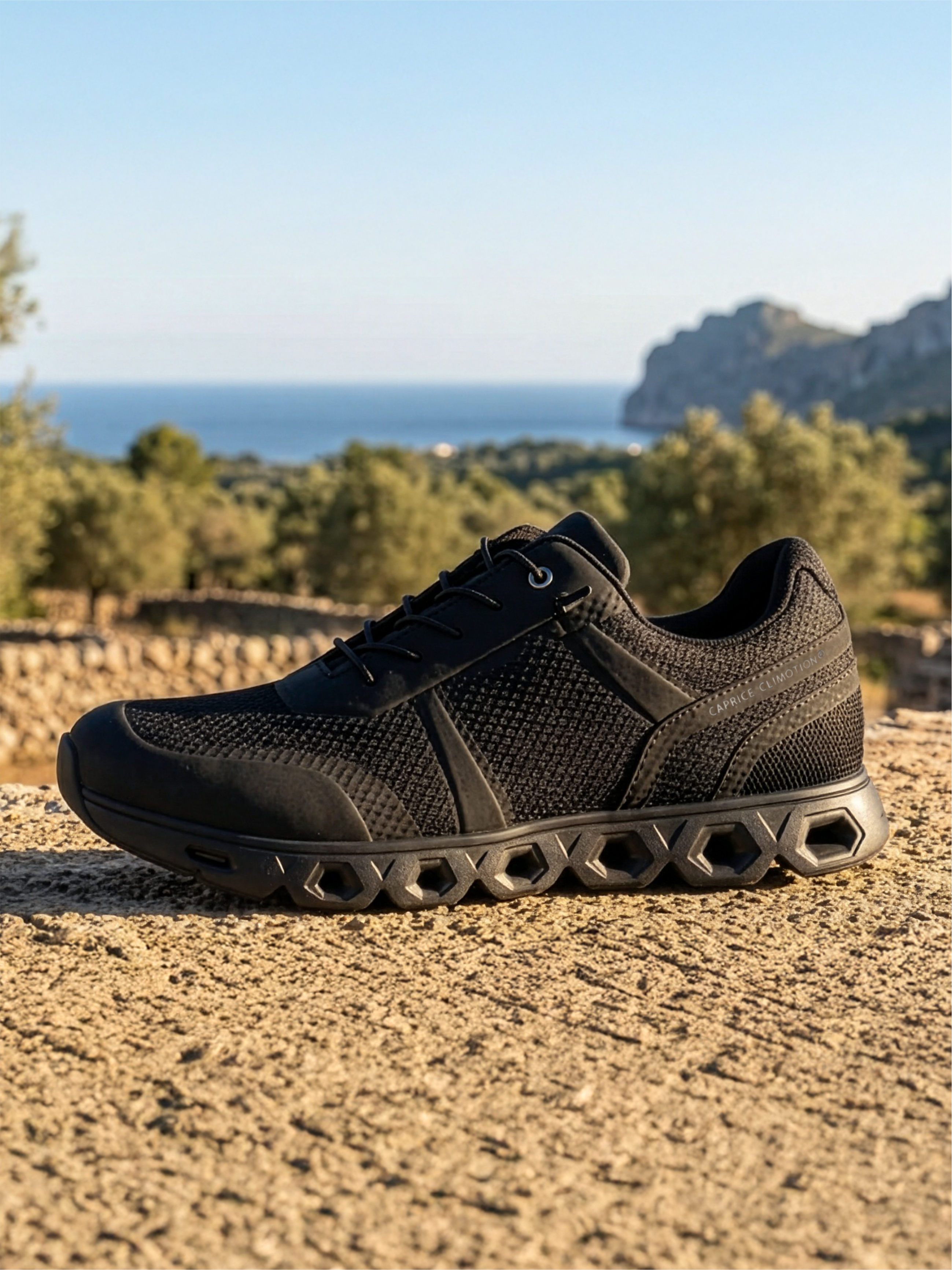 Black sports shoe with textured sole on stone wall, sea and coastal rocks in the background