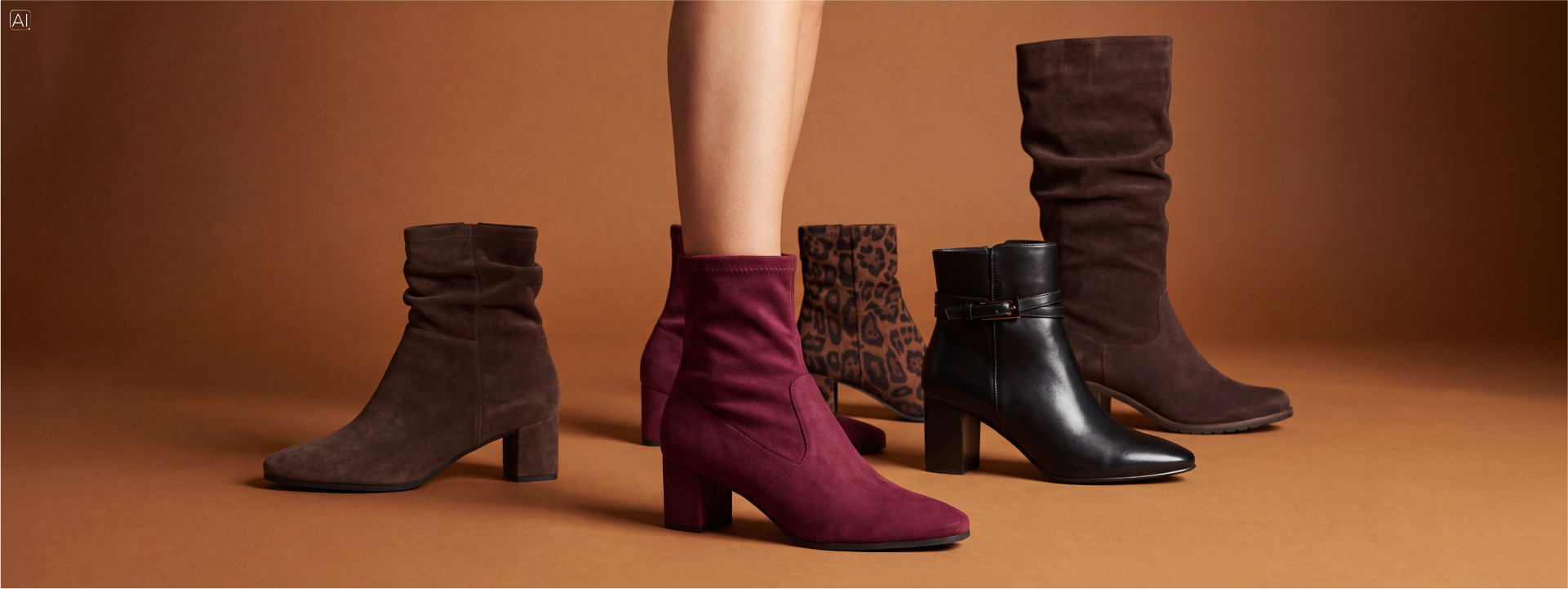 Fünf Damenstiefel in Braun, Bordeauxrot, Schwarz und Leopardenmuster vor einem warmbraunen Hintergrund, darunter ein bordeauxroter Stiefel am Fuß eines Models.
