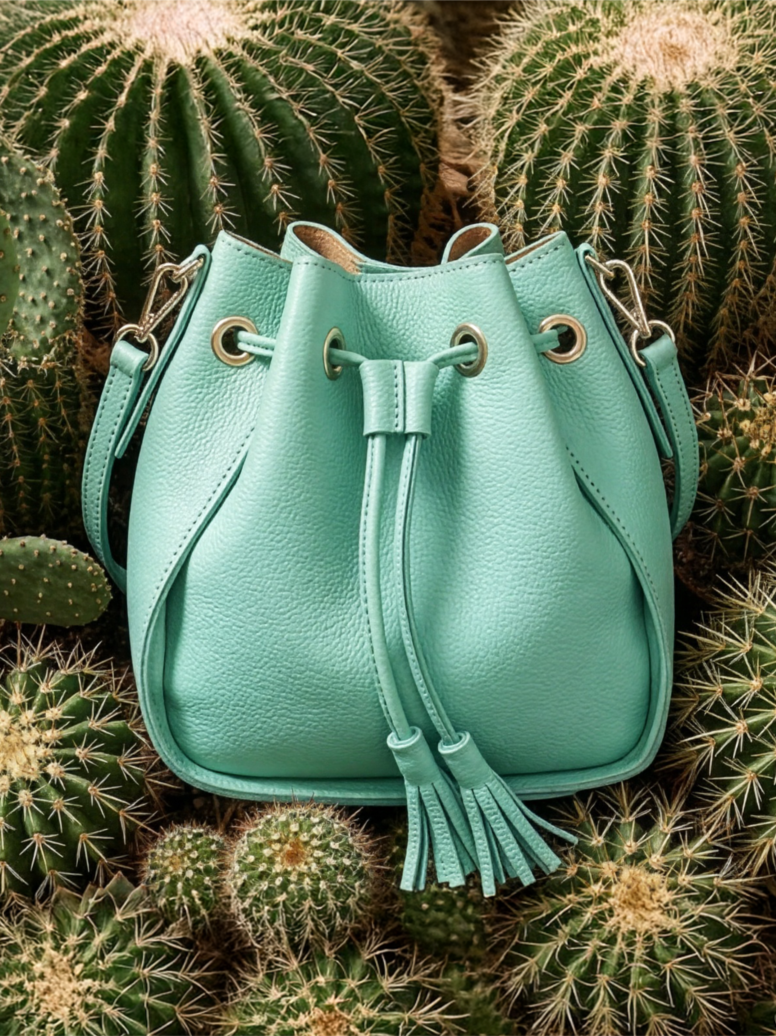 Borsa a marsupio in pelle verde menta con coulisse e nappe su uno sfondo di cactus e piante grasse.