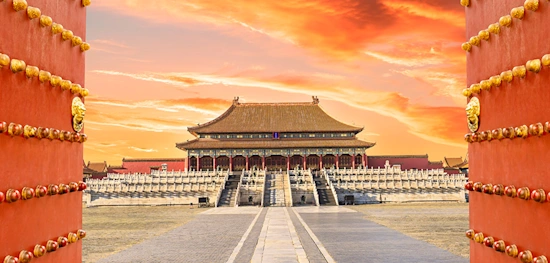 Picture of the Forbidden City in Beijing China during the sunset with a bright orange sky.