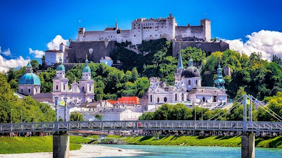 A scenic landscape picture of the Hohensalzburg Fortress and Salzach River in Salzburg (Austria), with clear blue skies 